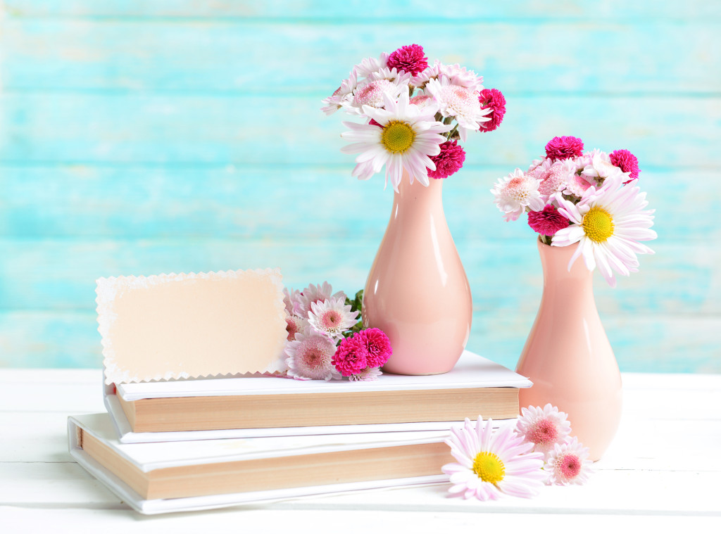 Beautiful flowers in vases on table on light blue background