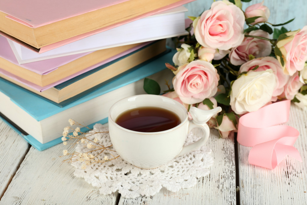 Cup of tea with books and flowers on wooden background